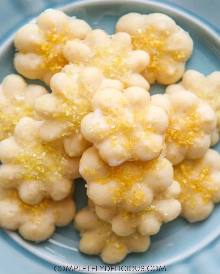 Lemon spritz cookies arranged on a plate with lemon slices