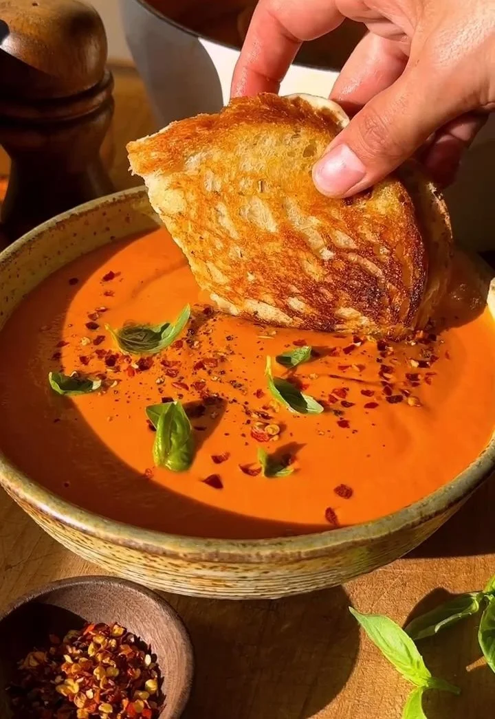 Bowl of middle-of-winter creamy tomato soup garnished with basil and bread
