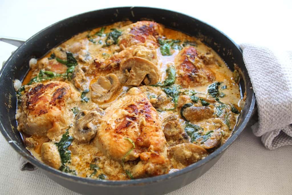 Plate of creamy spinach and mushrooms chicken garnished with herbs