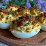 Creamy deviled eggs with bacon and chives on a serving platter