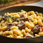 Plate of creamy steak pasta garnished with herbs and served with parmesan cheese.