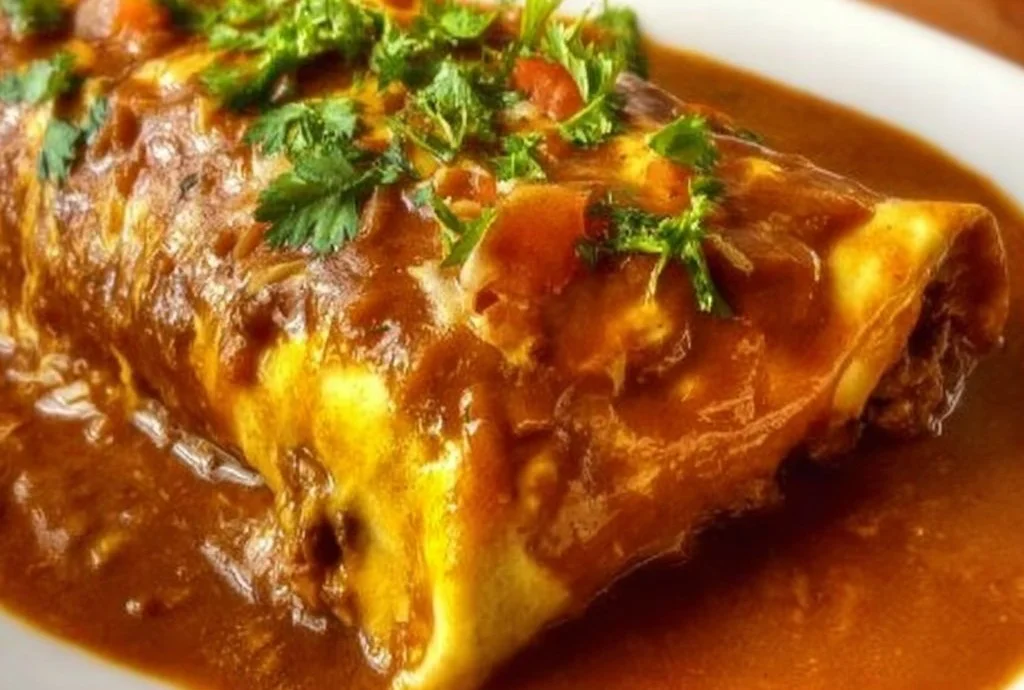 Delicious saucy ground beef wet burrito topped with cheese and fresh garnishes